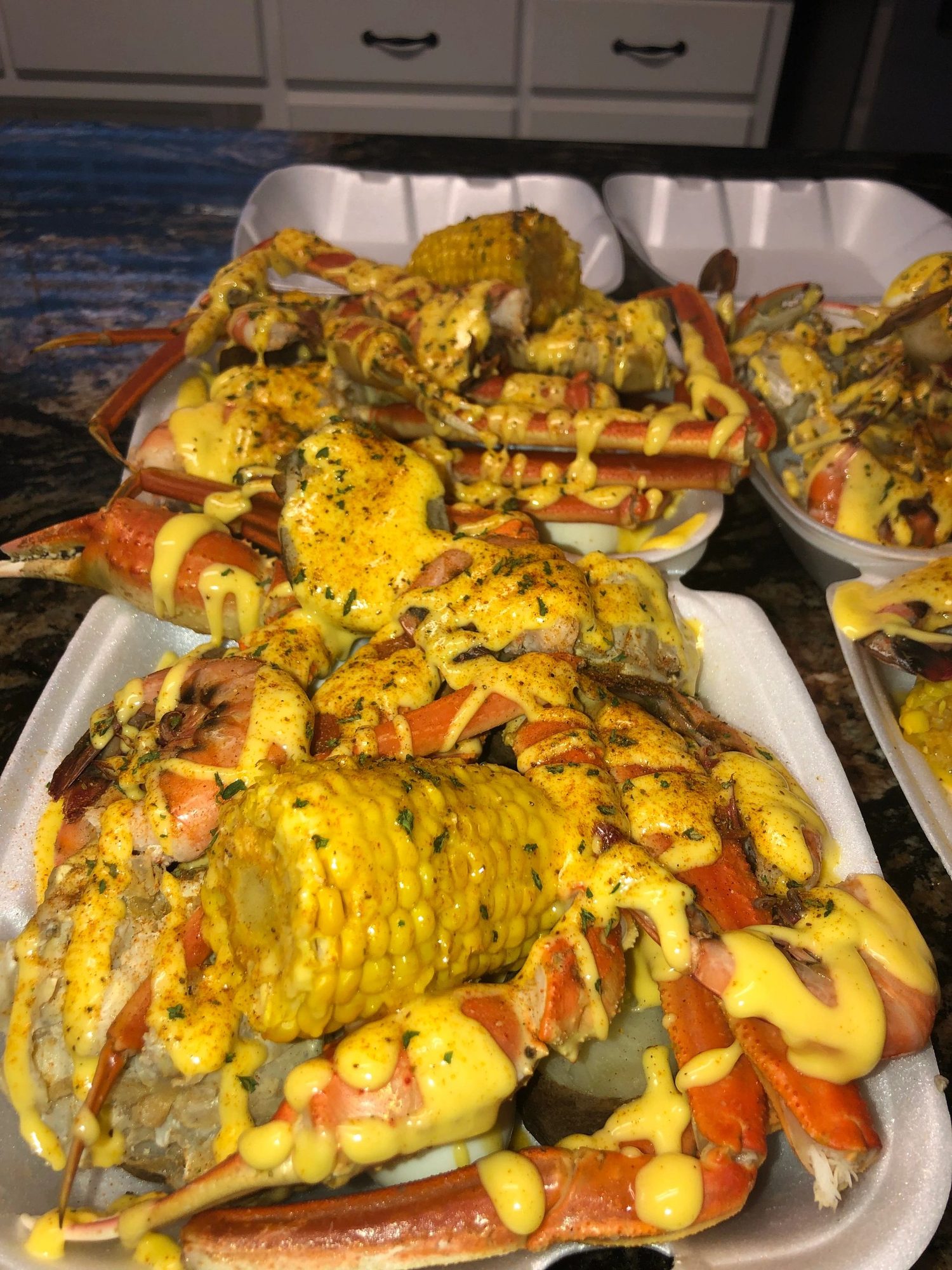 Takeout trays of snow crab and corn covered in Trap Butter